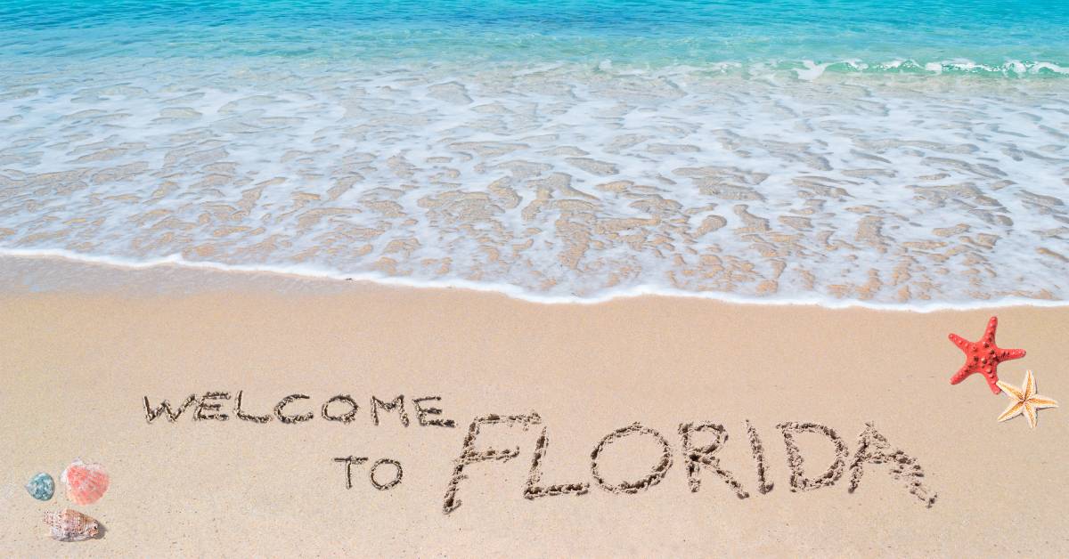 A welcoming message written in the sand at a beautiful Florida beach near the blue ocean on a sunny day.