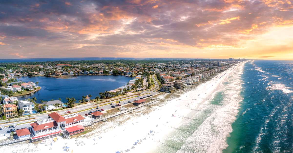 Miramar Beach in Destin, FL, in panorama. There are no people on the beach, but beach houses dot the road around the coast.