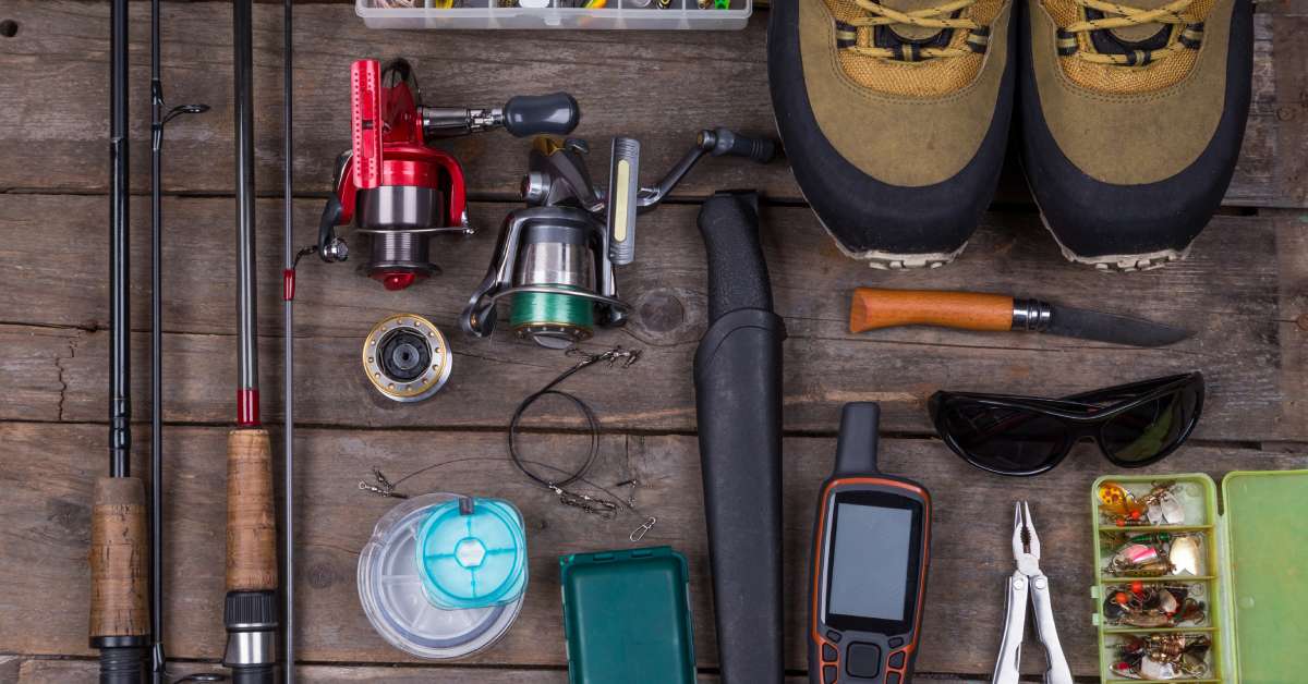 Fishing gear and tackle on a dark brown wooden table. The supplies on the table also include sunglasses.