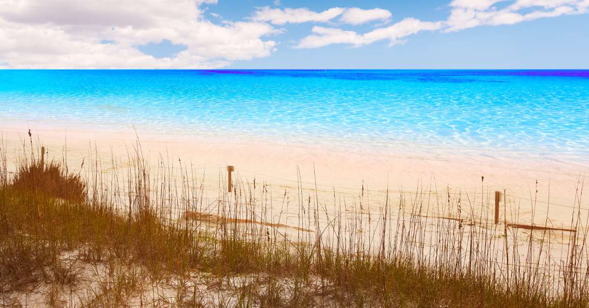 A sunny day on a beach in Destin, Florida. Some clouds are in the sky, and the water is crystal blue.