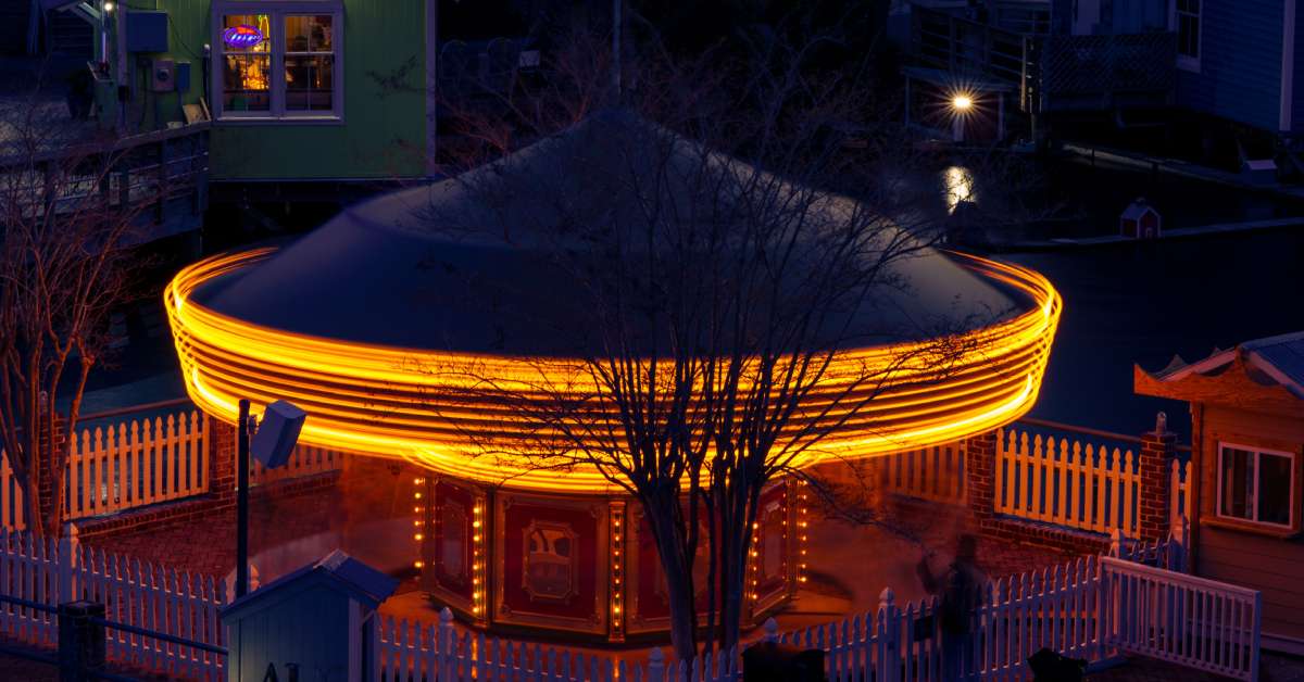 A dome-shaped building with lights on the roof at night. A green building with a "The Lazy Gecko" sign in the back.
