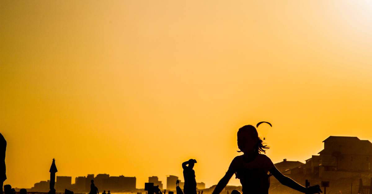 As the sun sets over a beach, people linger in quiet enjoyment. Their silhouetted figures create a serene scene.