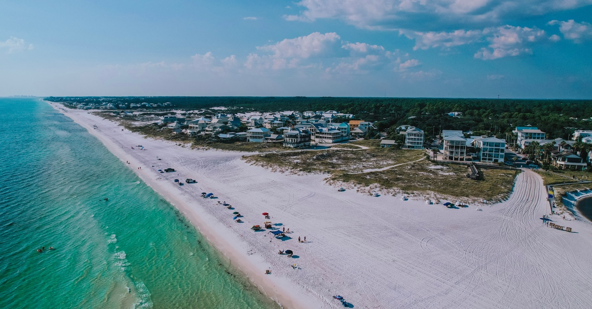 An aerial view of a strip of Grayton Beach, Florida, on a clear, sunny day. Several beachgoers dot the sand.